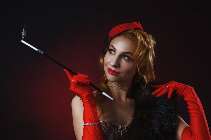 Victoria in a dramatic red burlesque outfit with a long cigarette holder