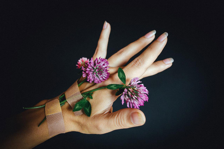 A photo of a hand posed with small wildflowers bandaged to it.